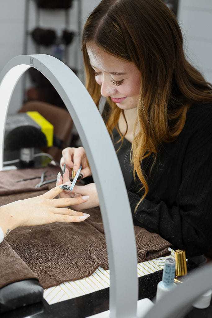 Woman receiving a manicure in a nail salon under bright light.