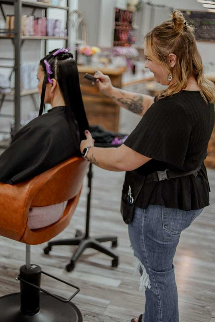 Stylist straightening a client's long hair in a salon chair.