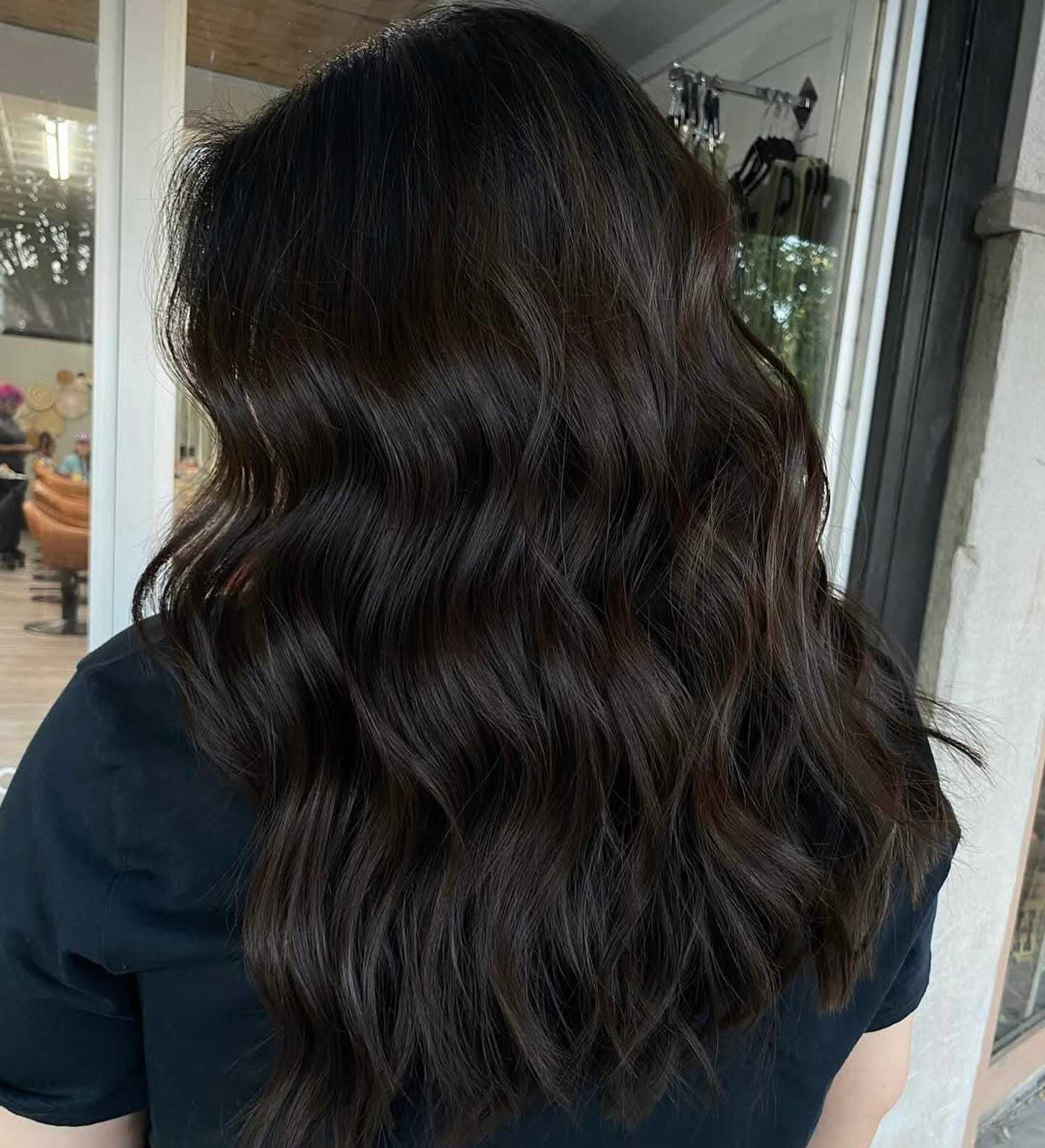Wavy brown hair styled in loose curls, viewed from the back in a salon setting.