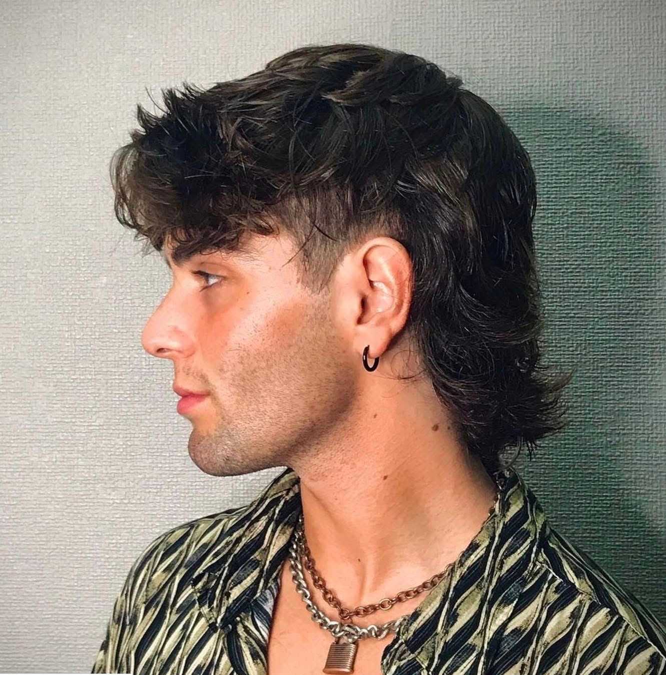 Man with mullet hairstyle, wearing hoop earring, zebra-patterned shirt, and chain necklace.