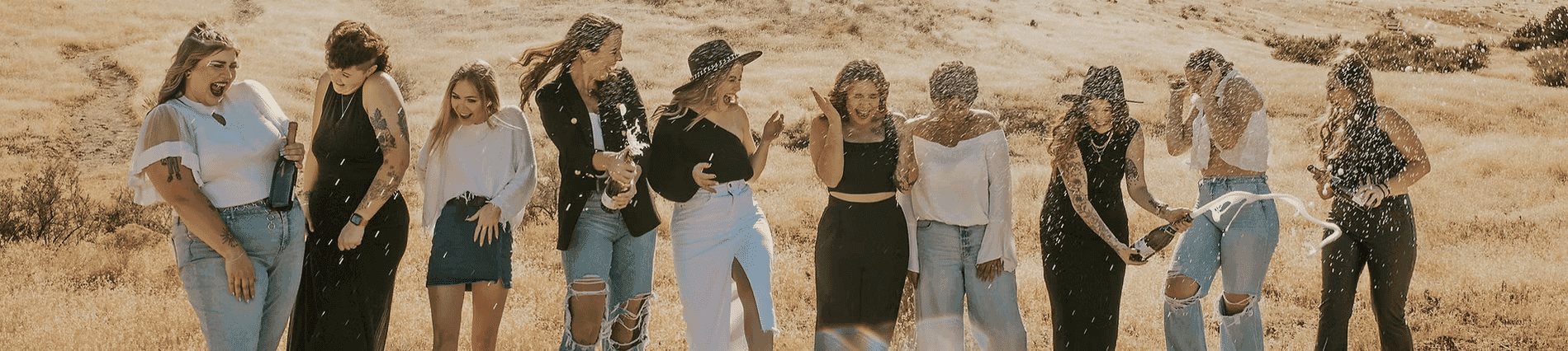 Group of women having fun, laughing, and splashing water in a sunny field.